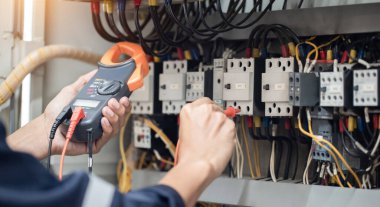 Elektrik mühendisi elektrik kabinesi kontrolündeki voltaj ve elektrik akımını ölçen bir testçi, elektrik sisteminin işleyişini konsept olarak kontrol ediyor .