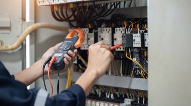 Elektrik mühendisi elektrik kabinesi kontrolündeki voltaj ve elektrik akımını ölçen bir testçi, elektrik sisteminin işleyişini konsept olarak kontrol ediyor .
