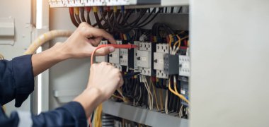 Elektrik mühendisi elektrik kabinesi kontrolündeki voltaj ve elektrik akımını ölçen bir testçi, elektrik sisteminin işleyişini konsept olarak kontrol ediyor .
