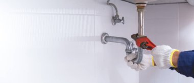 Tesisatçı ayarlanabilir anahtarla beyaz lavabo borusunu tamir ediyor..