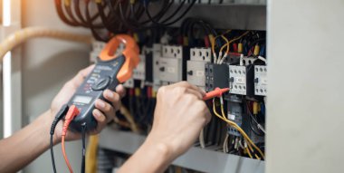 Elektrik mühendisi elektrik kabinesi kontrolündeki voltaj ve elektrik akımını ölçen bir testçi, elektrik sisteminin işleyişini konsept olarak kontrol ediyor .