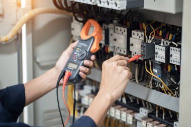 Elektrik mühendisi elektrik kabinesi kontrolündeki voltaj ve elektrik akımını ölçen bir testçi, elektrik sisteminin işleyişini konsept olarak kontrol ediyor .