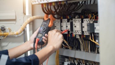 Elektrik mühendisi elektrik kabinesi kontrolündeki voltaj ve elektrik akımını ölçen bir testçi, elektrik sisteminin işleyişini konsept olarak kontrol ediyor .