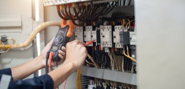 Elektrik mühendisi elektrik kabinesi kontrolündeki voltaj ve elektrik akımını ölçen bir testçi, elektrik sisteminin işleyişini konsept olarak kontrol ediyor .