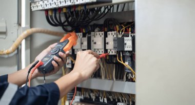 Elektrik mühendisi elektrik kabinesi kontrolündeki voltaj ve elektrik akımını ölçen bir testçi, elektrik sisteminin işleyişini konsept olarak kontrol ediyor .