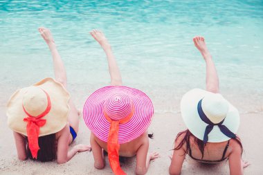 Seksi bikini vücudu. Üç Asyalı kadın kumsalda uzanmış şapkalarla denizin tadını çıkarıyorlar..