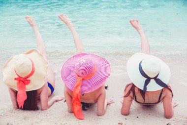 Seksi bikini vücudu. Üç Asyalı kadın kumsalda uzanmış şapkalarla denizin tadını çıkarıyorlar..