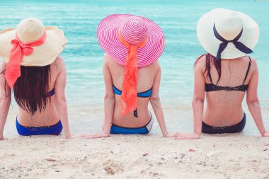 Seksi bikini vücudu. Üç Asyalı kadın kumsalda uzanmış şapkalarla denizin tadını çıkarıyorlar..