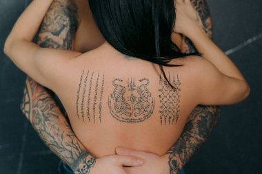 Bir erkek ve bir kadın sarılıyor. Çıplak üstsüz çift kucaklaşması. Ellerinde ve sırtında dövme olan bir kadın ve erkek. Seksi romantik randevu. Aşk.