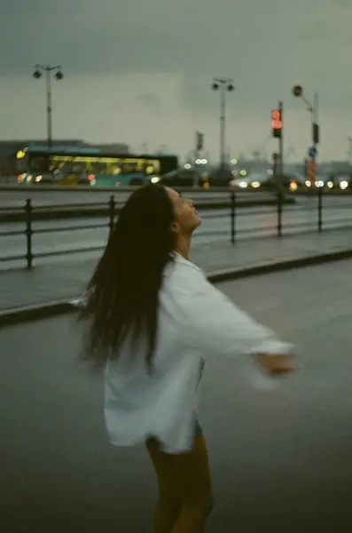 Yağmurlu bir havada sokakta yürüyen bir kadın. Beyaz gömlekli ve kot şortlu ıslak bir kadın. Yağmurlu bir şehirde esmer bir kız.