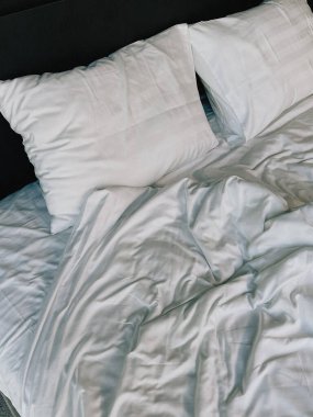 Beyaz yastıklı ve battaniyeli bir yatak. Yatak odası evde ya da tatil otelinde.