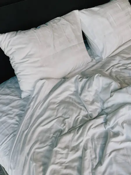 Beyaz yastıklı ve battaniyeli bir yatak. Yatak odası evde ya da tatil otelinde.