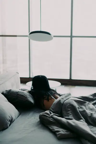 Yatakta yatan kadın. Gri yorganla kaplı, yatak odasında uyuyan çıplak genç bir kadın. Lüks ipek çarşaf. Esmer kız..