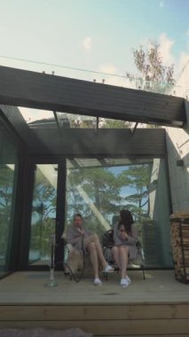 Güvertede bir sandalyede oturan kadın ve erkek. Terasta nargile içip kırmızı şarap içen bir çift. Açık havada gri bornoz giyen biri. Dikey