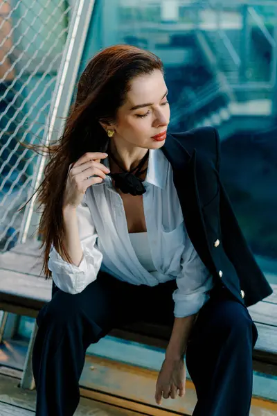 Siyah ceket ve güneş gözlüğü takmış şık bir kadın şehrin arka planına karşı şehir balkonunda kendine güvenen bir duruş sergiliyor şık ve sofistike bir görünüm sergiliyor.