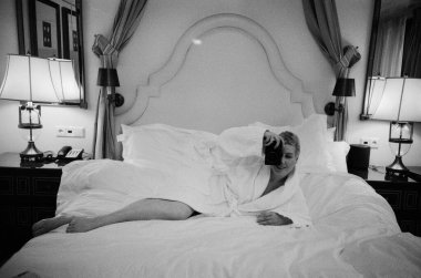 Beyaz bornozlu bir kadın rahat bir yatak odasında yatağa uzanıyor ve selfie çekiyor. Lüks otel odası sakin ve rahat bir atmosfer yaratıyor. Bu da onun yaşam tarzını güzelleştiriyor.