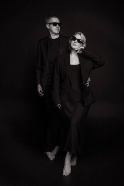 Şık ve modaya uygun bir çift siyah elbiseleriyle çarpıcı bir arka plana karşı zarif bir şekilde poz veriyor.