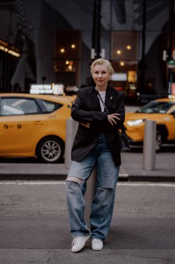Parlak sarı bir taksi geçerken, hareketli ve canlı bir şehirde büyük bir güvenle poz veren şık bir şahıs. New York 'lu Kadın.