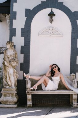 Güzel beyaz bir elbise giymiş şık bir kadın zarif bir şekilde klasik bir arka plana karşı poz verir.