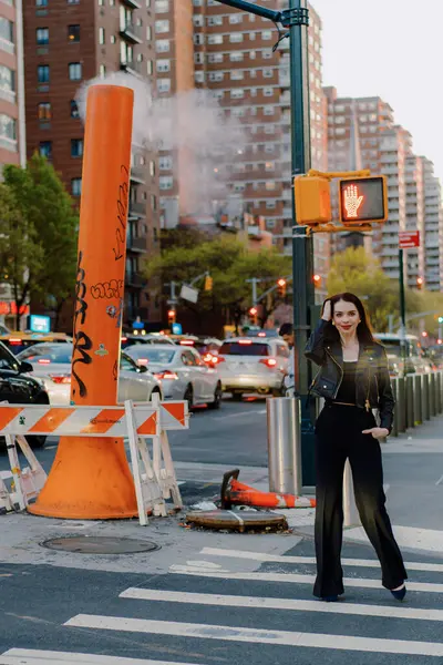 Şehir merkezindeki hareketli bir bölgede, şık bir kadın şehir manzarası zemininde, şehir içi yaya geçidinde güvenle yürüyor, modern ve bağımsız bir yaşam tarzı sergiliyor. New York