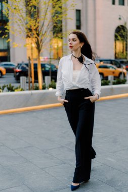 A successful businesswoman, dressed in a white blouse and black pants, exudes confidence and professionalism in the bustling city, symbolizing success and elegance in her corporate attire clipart