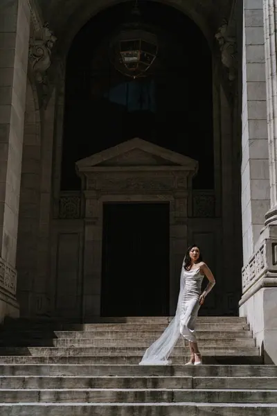 Şık bir elbise içinde muhteşem bir gelin büyük bir mimari arkaplanda akıcı bir perdeyle zarifçe poz verir..