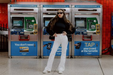 NEW YORK, ABD - 22 Nisan 2024: Şık ve modaya uygun bir kadın canlı ve hareketli bir metro istasyonunda ATM 'nin yanında güven içinde poz veriyor
