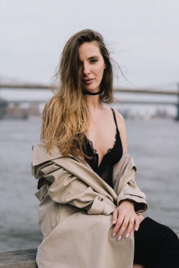 Suyun yanında zarif poz veren trençkotlu şık bir model zarafet ve şehir güzelliğinin bir karışımı..