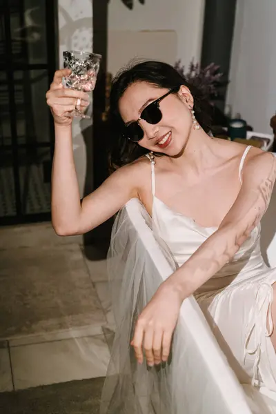 Şık bir kadın şık bir küvette dinleniyor, modaya uygun güneş gözlükleri takıyor ve ferahlatıcı bir içecek içiyor.