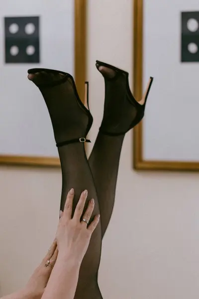 Şık bir fotoğraf siyah çoraplar ve yüksek topuklularla zarif poz veren bacakları modern dekor arka planına dokunarak, entellektüellik ve cazibe saçan ellerle yakalar.