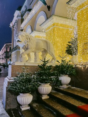 During the night, an impressive building is beautifully decorated with festive lights, a Lion statue, and elegant potted plants, creating a grand winter scene reflecting magnificence and charm clipart