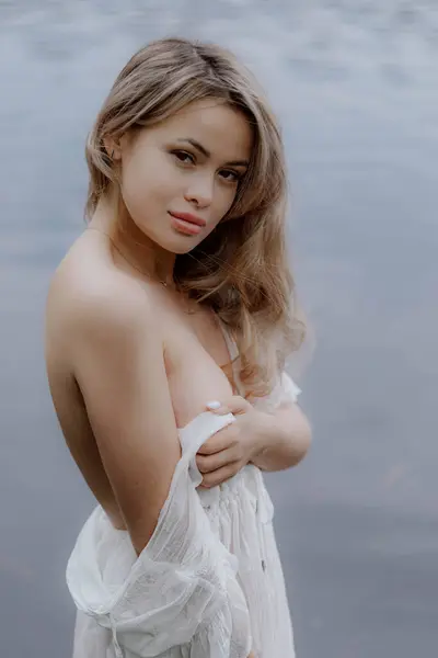 Suyun Huzurlu Vücudu pozunda, Beyaz Elbiseli Serene Kadını. Ormanda uzun ve şeffaf bir gelinlik giymiş kadın ya da gelin. Göl, gölet ya da deniz yakınlarındaki vahşi sahil. Yaz titreşimleri. Güzel kız..