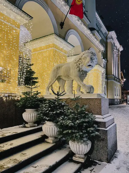 Bir gece fotoğrafında renkli ışıklarla aydınlatılmış ve bayraklarla süslenmiş tarihi bir bina ve çarpıcı bir aslan heykeli görülüyor. Karmaşık mimari zengin kültür mirasını yansıtıyor.