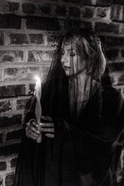 Eerie and captivating Portrait with dim Candlelight and a Veil. A haunting image of a solitary figure with a candle, against an intricately textured brick background. Witch at Halloween. clipart