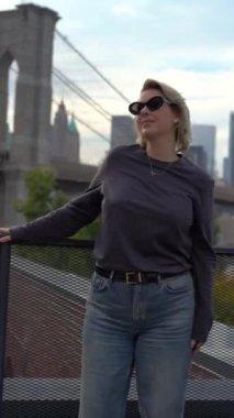 Moda düşkünü bir kadın Brooklyn Köprüsü 'nün yanında kendine güvenen bir poz verir. Şehir atmosferini hiç zorlanmadan somutlaştırır. New York