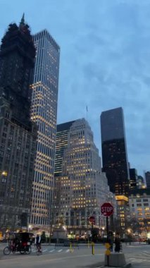 Aydınlatılmış gökdelenler ve hareketli bir meydan içeren New York şehrinin göz kamaştırıcı bir akşam manzarası..