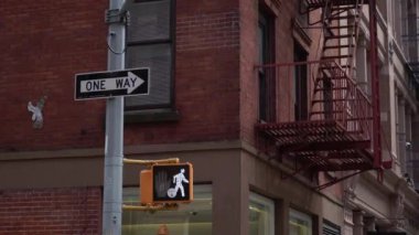 NEW YORK, ABD - 30 Mart 2024: Canlı bir şehir sahnesinde parlak bir yaya sinyali ve tuğla mimaride çarpıcı bir kırmızı yangın merdiveni yer alıyor