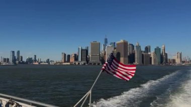 New York siluetinin nefes kesen manzarası. Önünde güzel bir Amerikan bayrağı var. Hepsi açık mavi gökyüzünün altında.