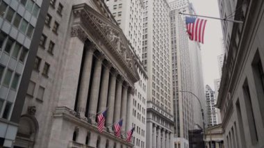 Wall Street 'in nefes kesici ve çarpıcı manzarası, ikonik mimarinin altını çiziyor ve Amerikan bayrağını sallıyor. New York Borsası Binası.