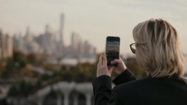 Akıllı telefonu ustalıkla kullanan biri gün batımında aydınlanan şehrin göz kamaştırıcı görüntüsünü yakalar. New York 'lu Kadın.