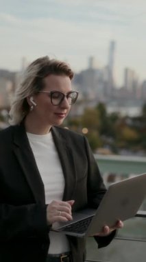 Profesyonel bir kadın şehir silueti arka planı olan, üretkenliği ve şehir yaşam tarzını somutlaştıran bir dizüstü bilgisayar kullanır..
