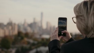 Akıllı telefonu ustalıkla kullanan biri gün batımında aydınlanan şehrin göz kamaştırıcı görüntüsünü yakalar. New York 'lu Kadın.