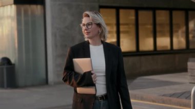 Şık bir iş kadını elinde dizüstü bilgisayarla dışarı çıkar ve modern profesyonelliği gösterir..