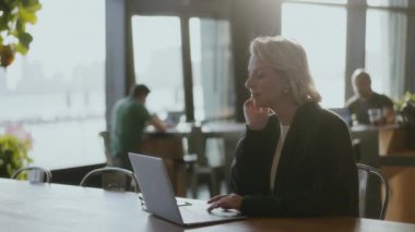 Modern bir çevrede üretkenlik gösteren şık bir kafede çalışan bir profesyonel. Siyah ceketli kadın ofiste dizüstü bilgisayar kullanıyor..