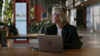 Modern bir çevrede üretkenlik gösteren şık bir kafede çalışan bir profesyonel. Siyah ceketli kadın ofiste dizüstü bilgisayar kullanıyor..