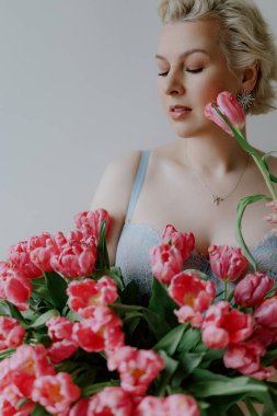 Zarif bir kadın zarif ve canlı pembe lalelerle poz verir yumuşak, rüya gibi bir arkaplana karşı. Mavi iç çamaşırlı bir kadın..