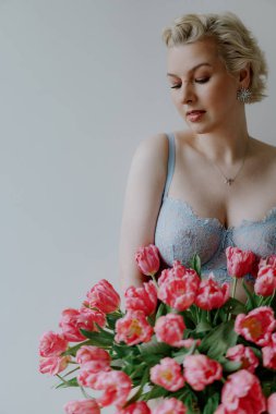 A graceful woman elegantly poses with a stunning and vibrant bouquet of pink tulips against a soft, dreamy backdrop. Female in blue underwear bra. clipart