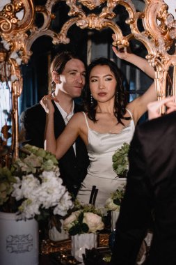 Resmi giyinmiş şık bir çift, çiçeklerle çevrili göz alıcı bir etkinlikte aynı anı paylaşır. Gelin ve damat düğün gününde