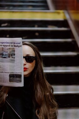 NEW YORK, ABD - 22 Nisan 2024: Modaya uygun bir kadın, kent tarzı ve çağdaş yaşamı gözler önüne seren bir gazetenin arkasında yüzünü gizliyor.