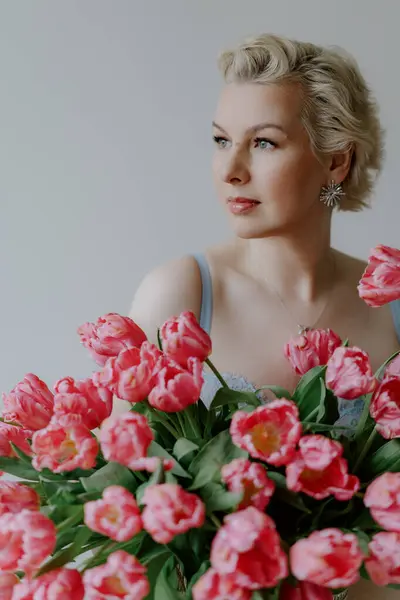 Zarif bir kadın zarif ve canlı pembe lalelerle poz verir yumuşak, rüya gibi bir arkaplana karşı. Mavi iç çamaşırlı bir kadın..